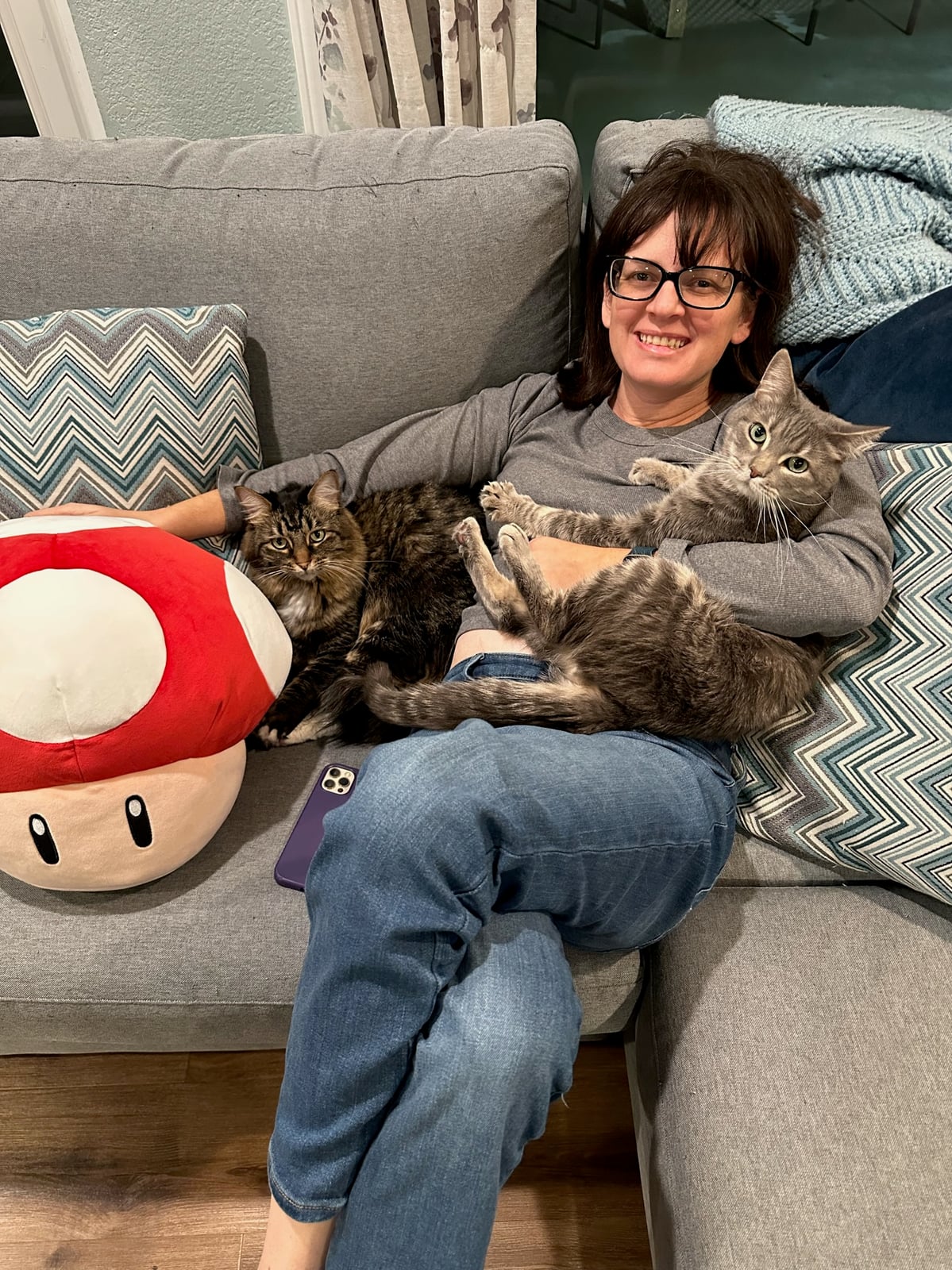 KT on the couch with both cats curled up on her